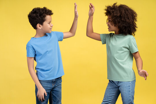 Two small kids giving high five and smiling to each other while posing in studio. Friendship concept