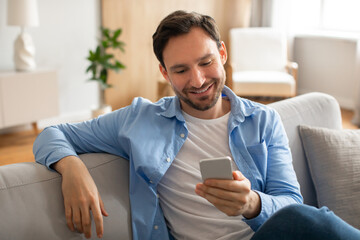 Man Sitting on Couch Looking at Cell Phone