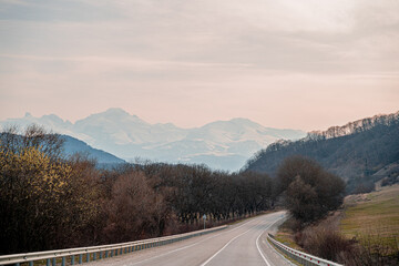 the road to the right is an asphalted picturesque road with a turn to the right into the mountains with a view of the snow-capped tops of the mountains and a blue sky with clouds and along the road th