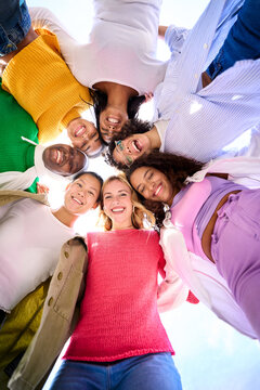 Vertical Low angle of a group of multiracial young only women looking at camera standing in a circle smiling and hugging each other. Female people embracing together having fun and enjoying friendship