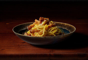 Spaghetti carbonara in dark bowl on wooden table