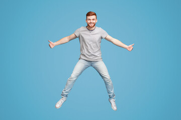 Young millennial guy jumping in air, demonstrating thumbs up gesture