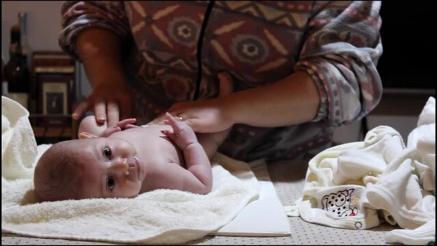 A white Caucasian mother changing and wiping her new-born baby on a nappy changer table top - sideways panning camera motion