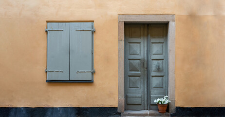 Wooden closed gray window and grey door with potted plant on orange wall background Stockholm Sweden