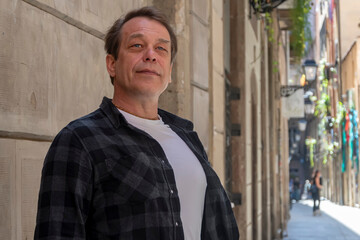 A smiling middle-aged man of sturdy build stands near a wall in the street.
