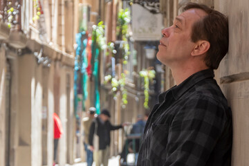 An elderly man leans his head against a wall in a city alley and looks up.