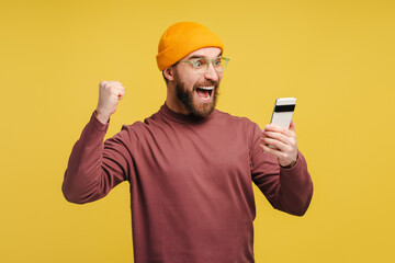 Portrait of excited man holding mobile phone, watching video making victory gesture