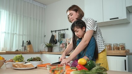 Smart caucasian mother and asian girl cooking together and chopping vegetable or preparing salad...