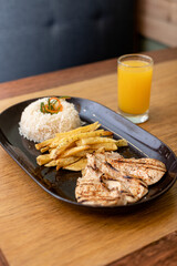 Grilled chicken, accompanied by rice, French fries and orange juice.
