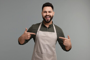 Happy man pointing at kitchen apron on grey background. Mockup for design