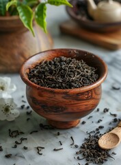 Black tea leaves in a wooden bowl with a wooden spoon and white flowers