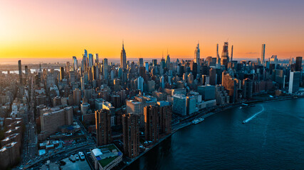 Orange light of setting sun illuminating the skyscrapers and high-rise buildings in New York scenery. Top view on the metropolis from above the East River.