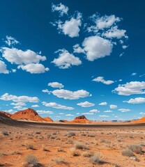 Naklejka premium Arid desert landscape with red rock formations under a blue sky with white clouds