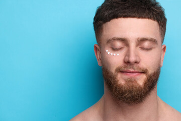 Handsome man with moisturizing cream on his face against light blue background, space for text