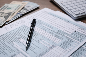 Payroll. Tax return forms, pen, dollar banknotes and calculator on table, selective focus