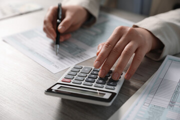 Payroll. Woman using calculator while working with tax return forms at wooden table, selective focus