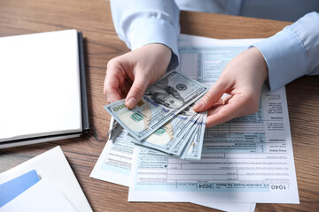 Payroll. Woman with dollar banknotes and tax return forms at wooden table, closeup