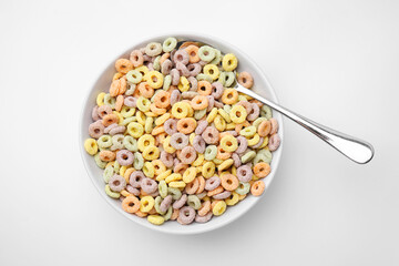 Tasty cereal rings in bowl and spoon on white table, top view