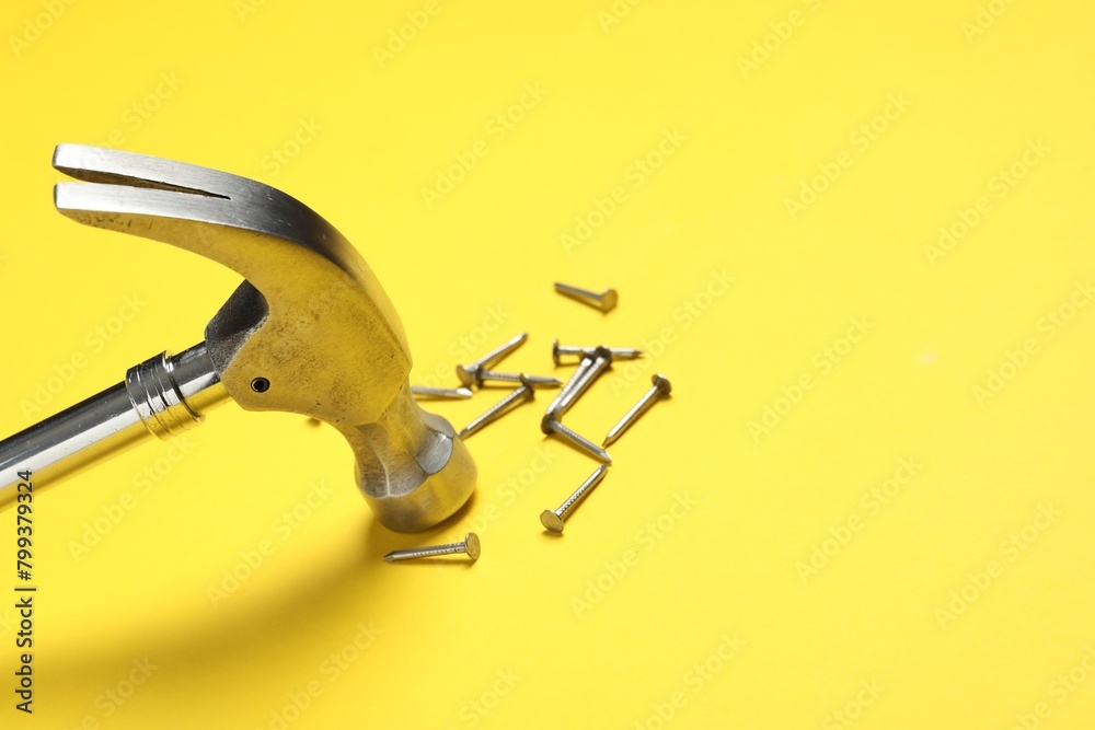 Poster Hammer and metal nails on yellow background, closeup. Space for text