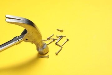 Hammer and metal nails on yellow background, closeup. Space for text
