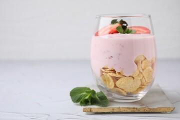 Glass with yogurt, strawberries and corn flakes on white textured table. Space for text