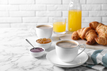 Tasty breakfast. Cups of coffee, fresh croissants and jam on white marble table, space for text