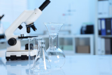 Laboratory analysis. Different glassware and microscope on white table indoors, closeup. Space for...