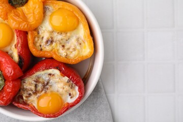Delicious stuffed peppers with eggs in bowl on white tiled table, top view. Space for text