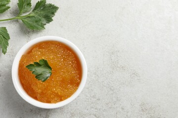 Fresh pike caviar in bowl and parsley on light grey table, top view. Space for text