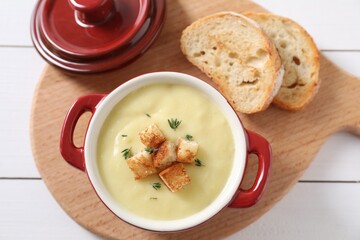 Tasty potato soup with croutons and rosemary in ceramic pot on white wooden table, flat lay