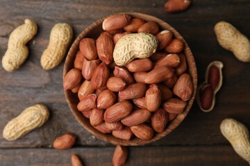 Fototapeta premium Fresh peanuts in bowl on wooden table, flat lay