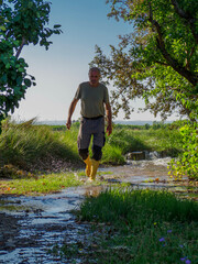 Older man in boots irrigating a field of fruit trees
