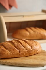 Wooden bread basket with freshly baked loaves on white marble table in kitchen