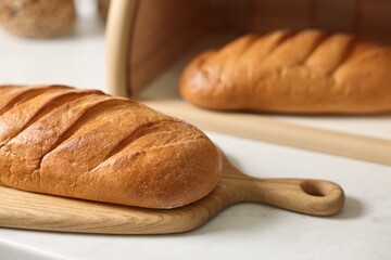 Wooden bread basket with freshly baked loaves on white marble table in kitchen, closeup