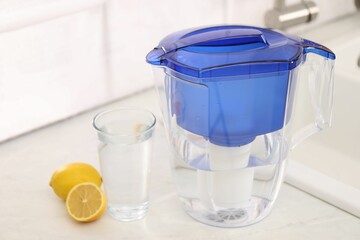 Water filter jug, glass and lemons on countertop in kitchen