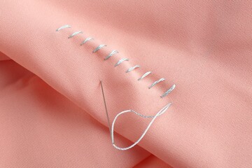 Sewing needle with thread and stitches on coral cloth, closeup