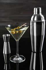 Metal shaker, Martini cocktail and jigger on black mirror surface