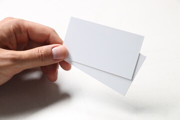 Man holding blank cards at white table, closeup. Mockup for design