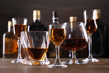 Different delicious liqueurs in glasses and bottles on wooden table