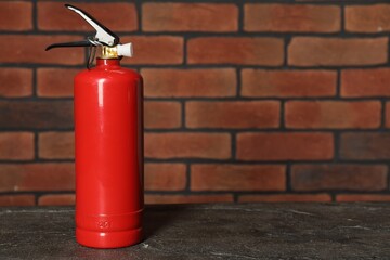 One red fire extinguisher near brick wall, space for text