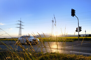 beautiful dramatic landscape, car road visible behind grass, power towers, field in evening in rays...