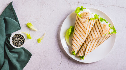 Grilled chicken fillet wrapped in tortilla with lettuce and sauce on a plate top view web banner