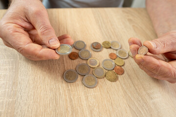 Senior man, poor pensioner lays out euro cent coins on wooden table, counts meager cash money on...
