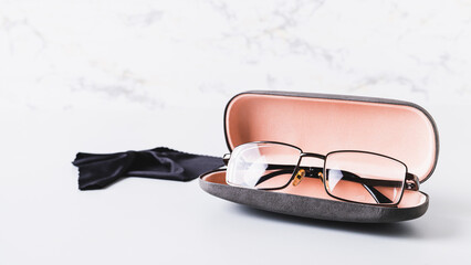 Eyeglasses in open hard case and cleaning cloth on table web banner