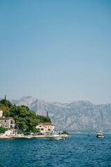 Fototapeta na wymiar Boats stand off the coast of Perast with old houses among green trees. Montenegro
