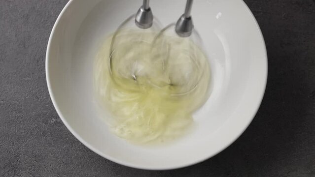 Chef whips raw egg whites in a white bowl with a mixer, top view. Close-up of food
