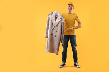 Dry-cleaning delivery. Happy courier holding coat in plastic bag on orange background, space for...