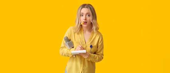 Portrait of busy female journalist with microphone taking notes on orange background