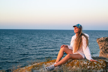 A woman with long hair sits on a stone on top of a mountain on the sea coast. Travel and tourism