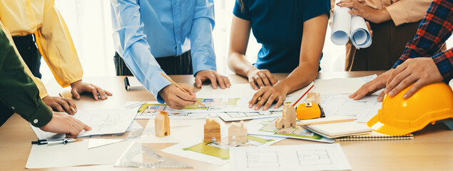 Professional architect engineer team discussion about architectural project on meeting table with wooden block and blueprint scatter around. Design and cooperate concept. Closeup. Delineation. - obrazy, fototapety, plakaty